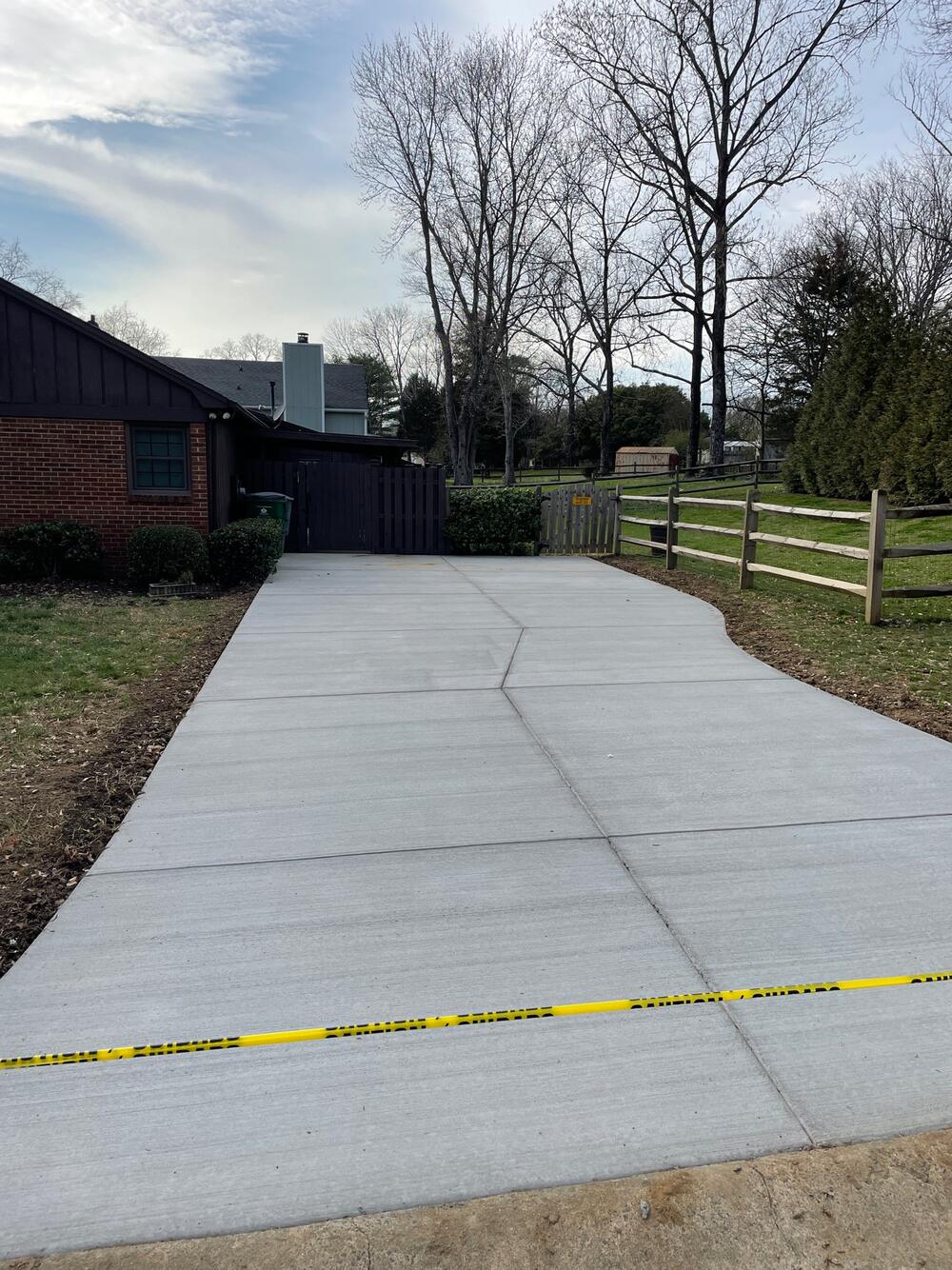 Newly poured broom-finished concrete driveway curving past a wooden fence