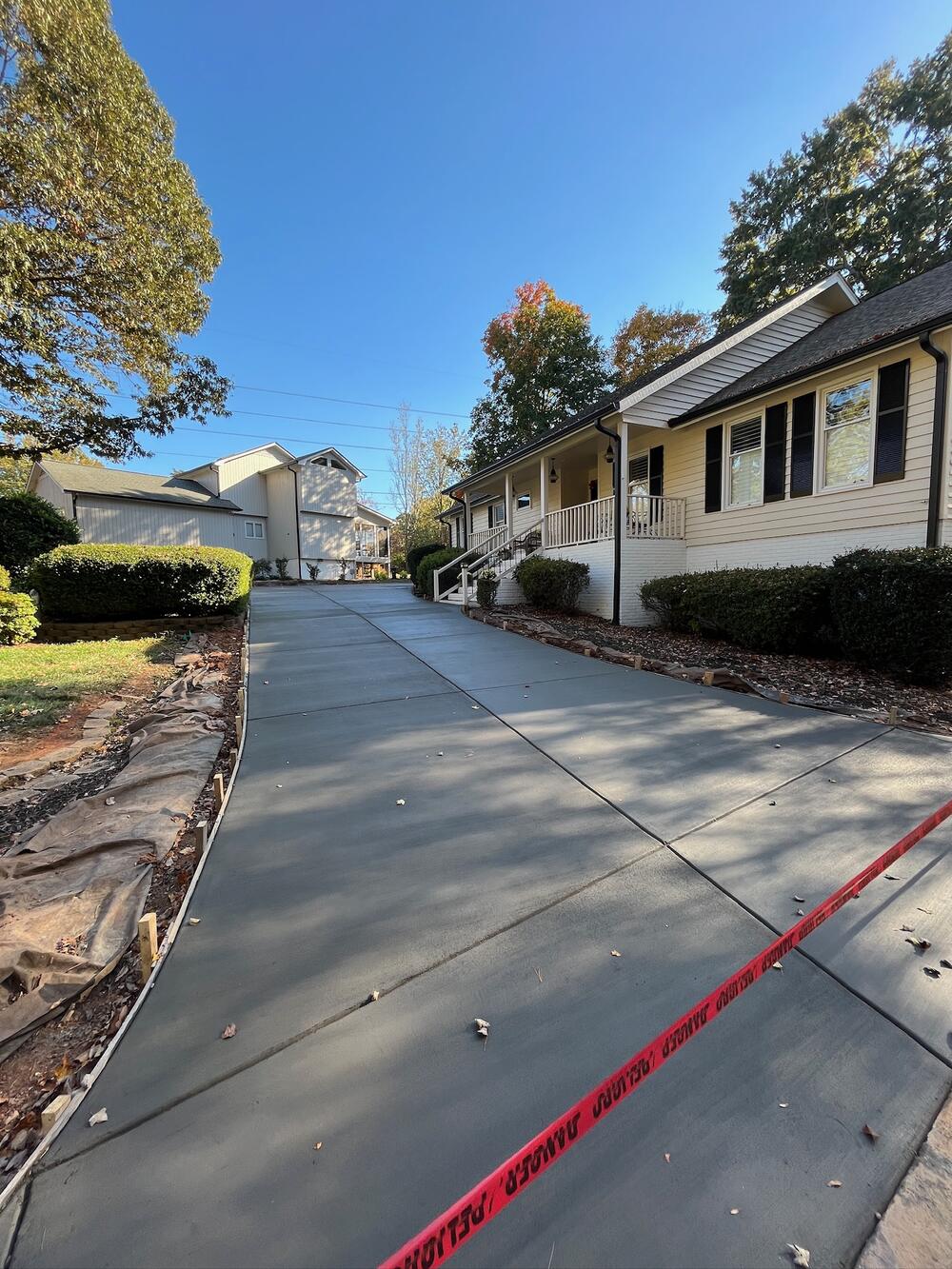 Long new concrete driveway beside a hillside with red caution tape